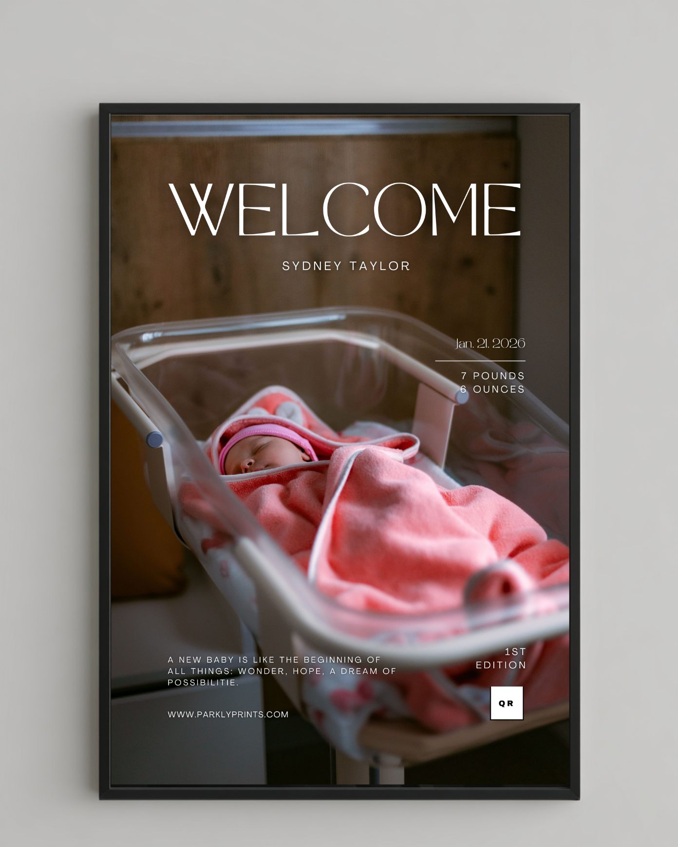 Framed poster with a newborn baby in a crib and text 'Welcome Sydney Taylor' on a gray wall.